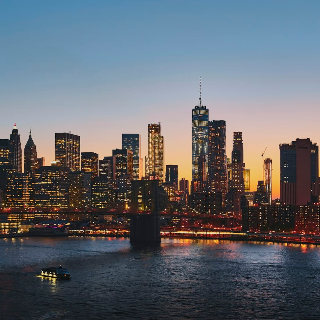Alacakaranlıkta ışıkları yanan Manhattan silueti ve önündeki nehir.